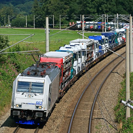 Eine Ellok der Baureihe 185 des EVU Lokomotion GmbH durchfährt mit einem Zug voller fabrikneuer Mercedes-Lkw zwischen Traunstei