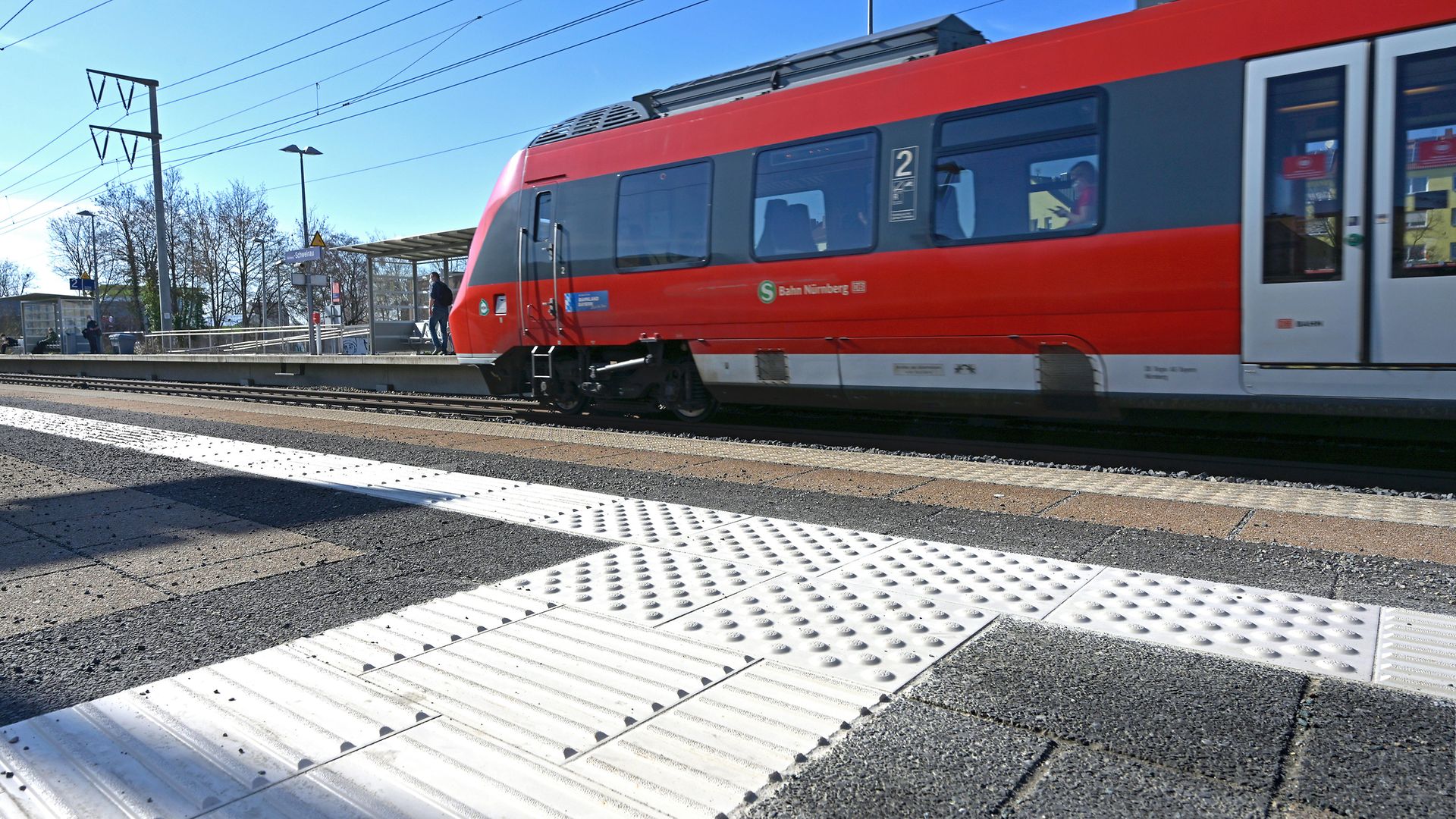 Taktiler Blindenleitstreifen auf dem Bahnsteig, ein haltender Zug im Hintergrund