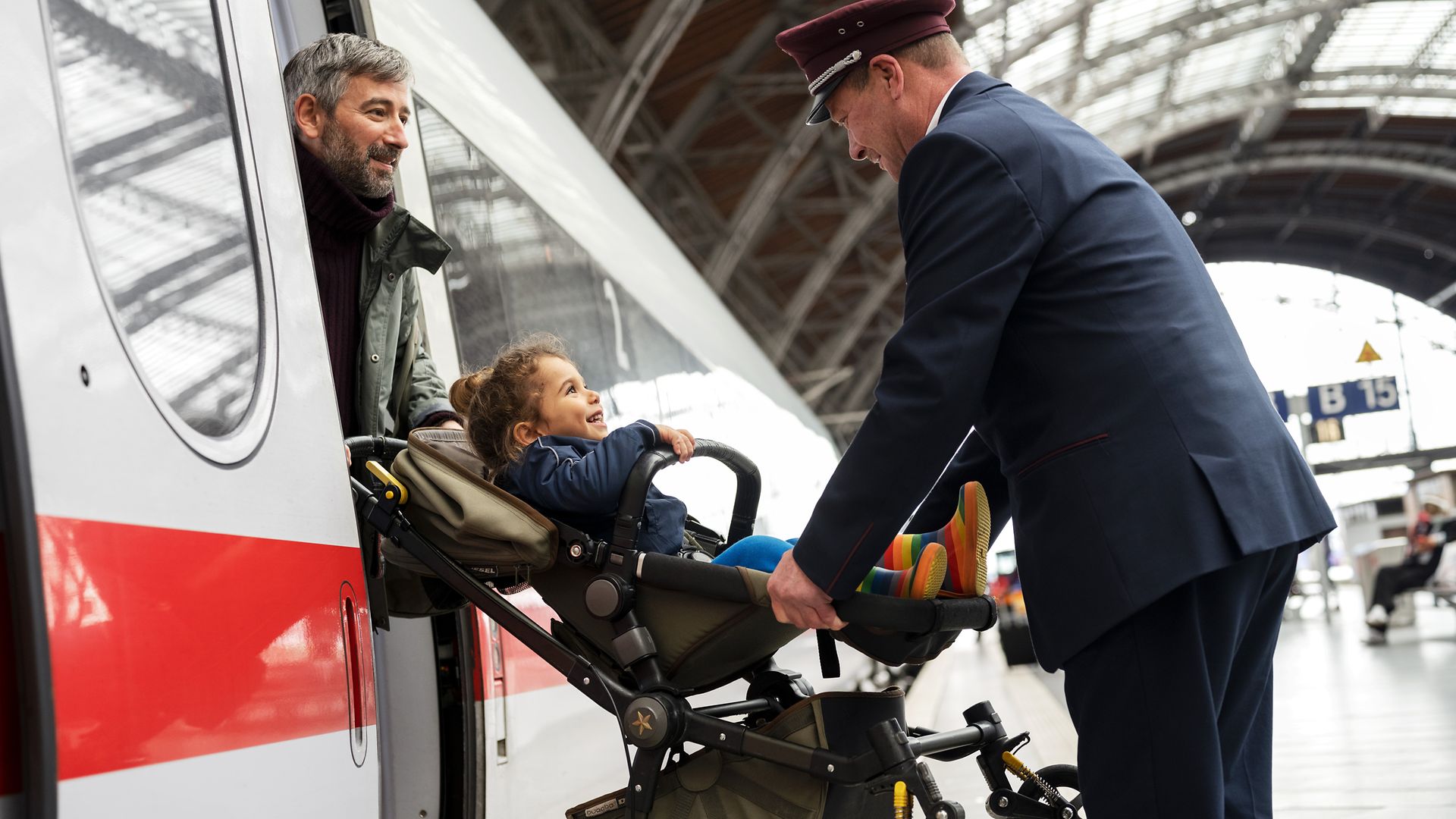 Ein Servicemitarbeiter hilft einem Vater mit Kinderwagen beim Ausstieg aus dem ICE