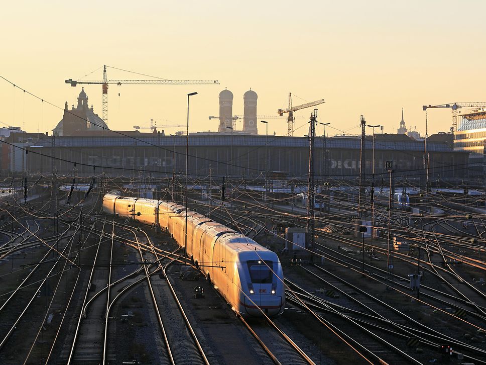 Der Blick auf Gleise und einen fahrenden ICE, im Hintergrund der Münchner Hauptbahnhof