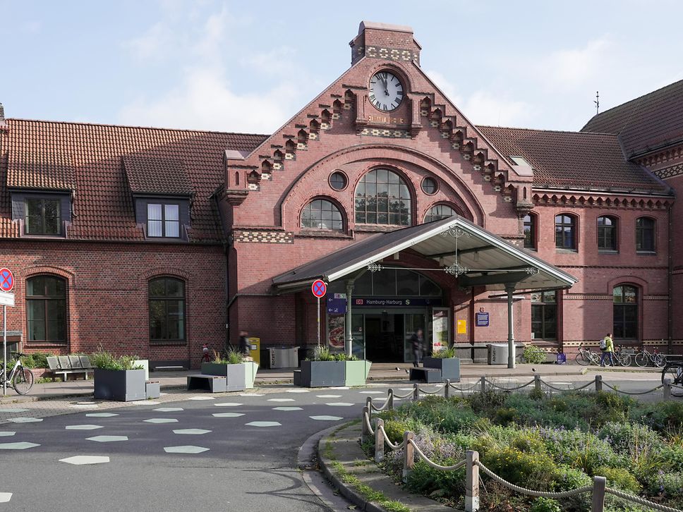 Ansicht auf Empfangsgebäude und Vorplatz eines Bahnhofs.